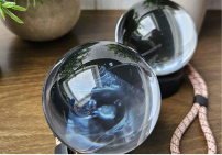 Two transparent glass spheres placed on a wooden surface, reflecting their surroundings with a braided cord nearby.